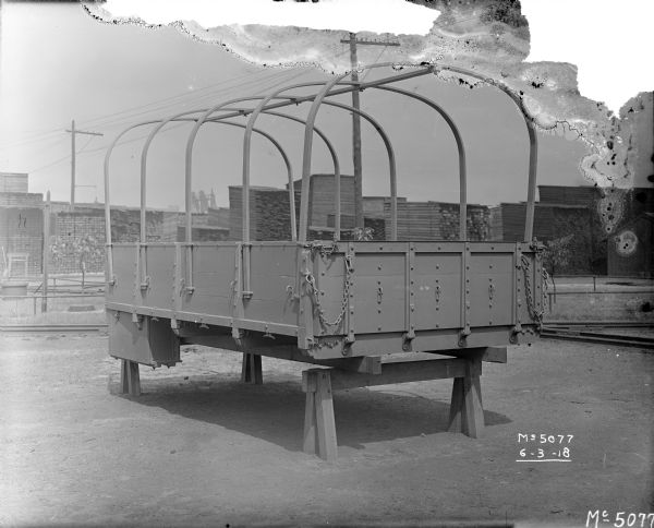 A truck frame for army use is set up on blocks in the yard at McCormick Works. The frame would be covered with a tarp. Railroad tracks and stacks of lumber are in the background. These WWI era trucks are sometimes referred to as "Liberty Trucks."