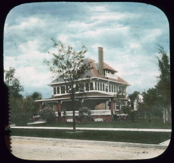 View from street towards a house in a residential neighborhood. Bushes are in bloom. Hand-tinted lantern slide.