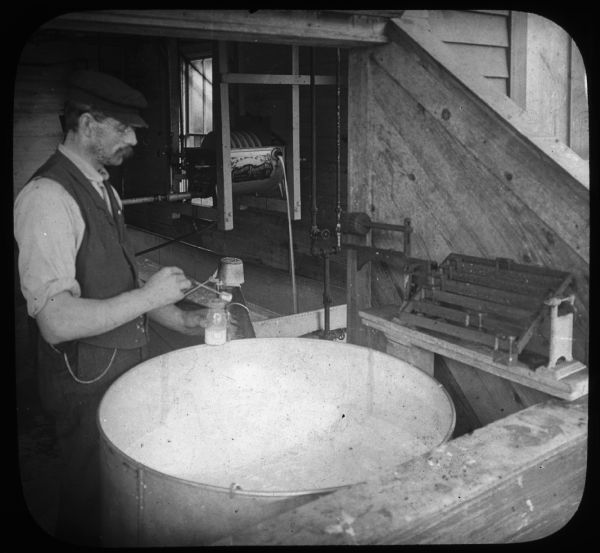 A man is weighing milk and taking a sample for testing in acid in butter fat, creamery, East Aurora, N.Y.., U.S.A." Lantern slide.