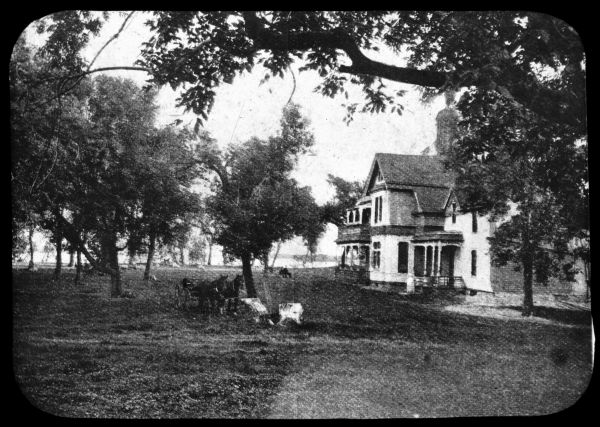House with yard and trees in rural settings. There is a team of two horses pulling a carriage. Lantern slide.