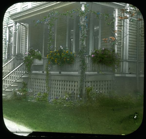 Flower boxes and vines growing on a front porch. Hand-tinted lantern slide.
