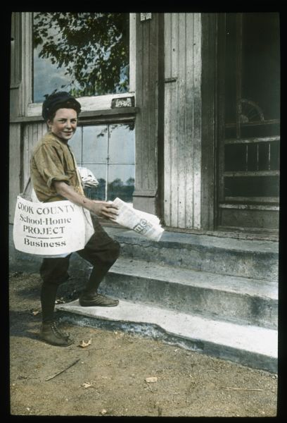 A boy is delivering a newspaper to the front step of a house. The sign on the newspaper bag reads: "Cook County School-Home Project — Business." Hand-tinted lantern slide.
