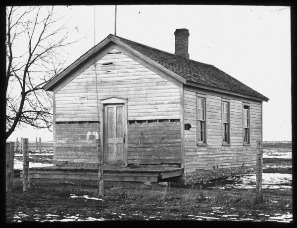 View of an old wooden schoolhouse in a rural winter setting. Lantern slide.