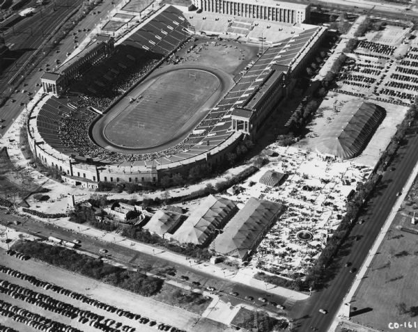 Original caption reads: "International Harvester's 8-acre exposition depicting 'Harvester's 100 Years in Chicago' shares space with famous Soldier Field on Chicago's lakefront in this striking aerial photo taken from the Goodyear blimp. A portion of the 73,000 Sunday crowd that jammed the exhibit on this sunny October day can be seen lined up to enter the historic 'Streets of Chicago' display. Outdoors in the gigantic tent is a showing of farm equipment, motor trucks and industrial power equipment, other thousands inspect many Harvester products. The exposition, continuing until November 2, marks the 100th anniversary of the erection of the first McCormick factory in Chicago."