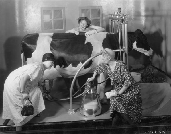 A group of three women are posing with a mechanical cow and milker in the International Harvester exhibit at the "A Century of Progress" world's fair.