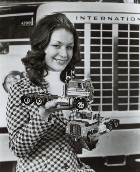 "Alter-Ego in Miniature." Portrait of a woman holding two miniature tractors. Typewritten copy reads: "The Famous International 4270 Conventional Transtar tractor now has an alter-ego in miniature. This 1/25th scale replica (bottom) faithfully captures every detail of its full size prototype. Made by the Ertl Company, Dyersville, Iowa, it is the second in a series which also includes the recently re-introduced CO-4070A Transtar tractor model (top). Each kit features over 250 molded plastic pieces, paint masks, key tab assembly and full instructions. Manufactured under license of International Harvester Company, the kits are available in IH dealerships and branches, and better toy and hobby shops."