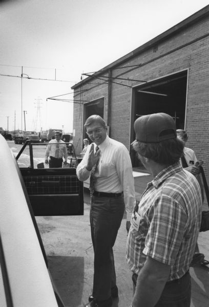 Warren Hayford's Tour of Fort Wayne Plant. People are standing outdoors near a vehicle, with an industrial building in the background.