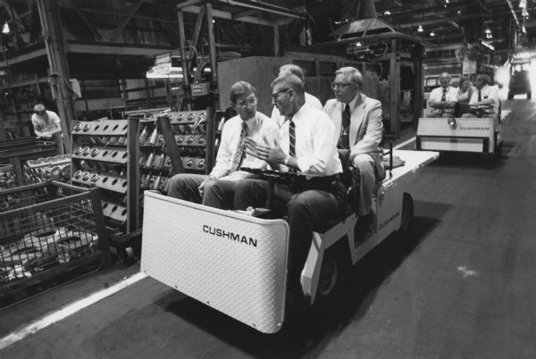 Warren Hayford's Tour of Fort Wayne Plant. Two groups of men are sitting in Cushman vehicles touring the inside of the factory.