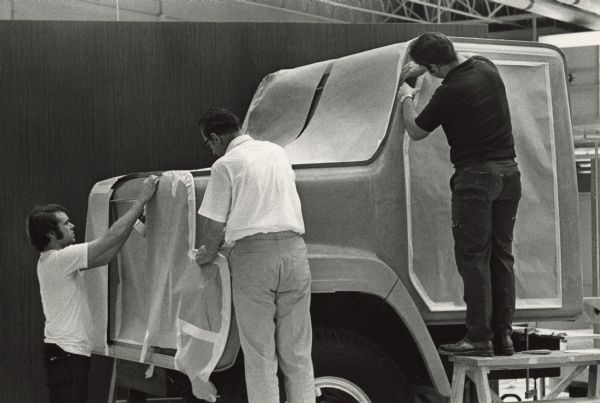 Three men are working on the development of a truck.