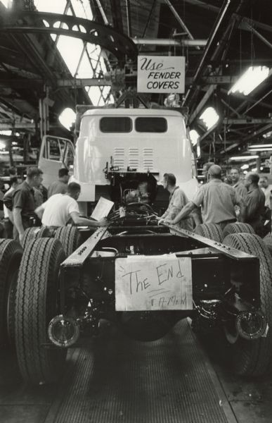Men working on factory floor with a truck. A sign on the back of the truck chassis reads: "The End."