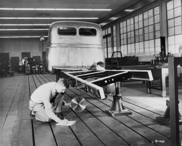 Two men are working indoors testing the chassis of a truck.