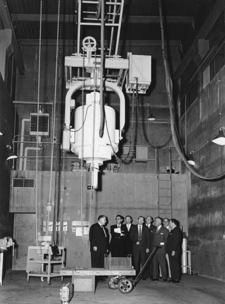 A group of men are standing underneath the X-ray machine which is suspended from the ceiling. Caption reads: "One Million Volt X-Ray Machine at Manufacturing Research."
