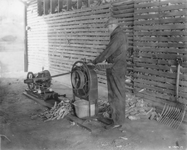 Farmer operating a McCormick-Deering corn sheller powered by a portable engine.