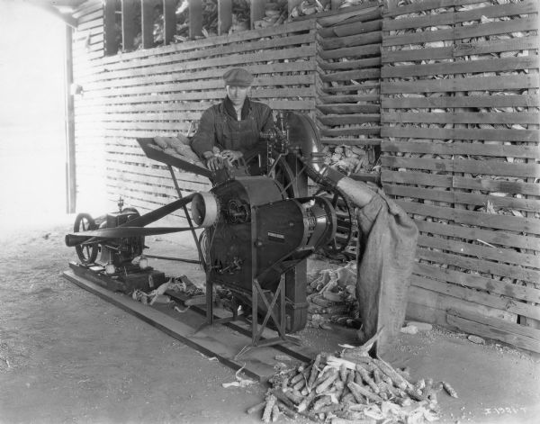 Farmer operating a McCormick-Deering corn sheller powered by a portable engine.
