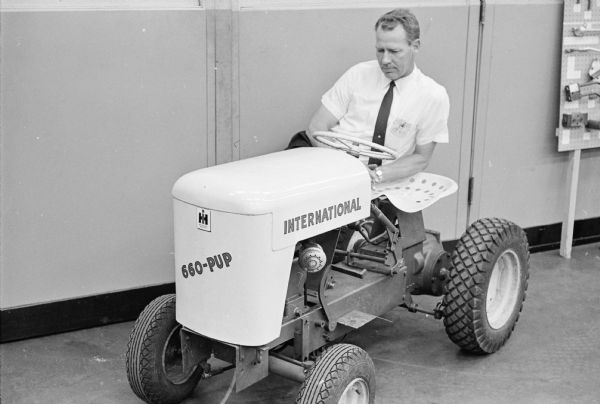 A man is crouching behind an International Cub Cadet lawn tractor marked "660-PUP" at the Louisville Works factory.