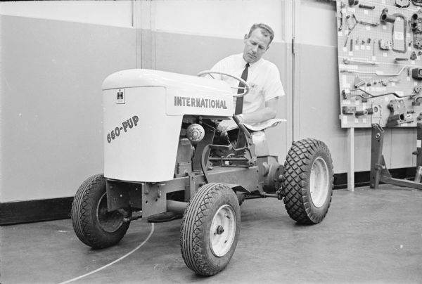A man is crouching behind an International Cub Cadet lawn tractor marked "660-Pup" at the Louisville Works factory.