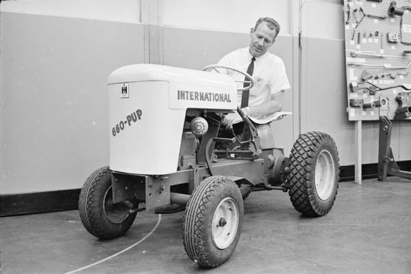 A man is crouching beside an International Cub Cadet lawn tractor marked "660-Pup" at the Louisville Works factory.
