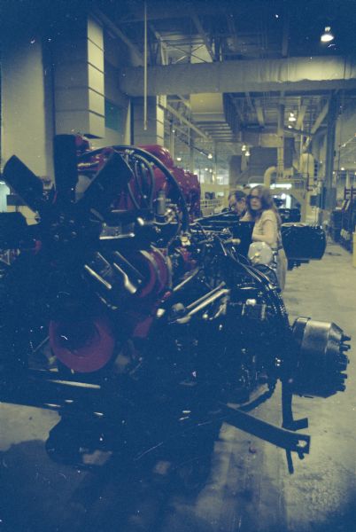 Engine in a factory. A man and woman are in the background.