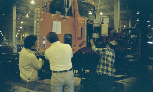 Three men are working near the cab of a truck in the factory.
