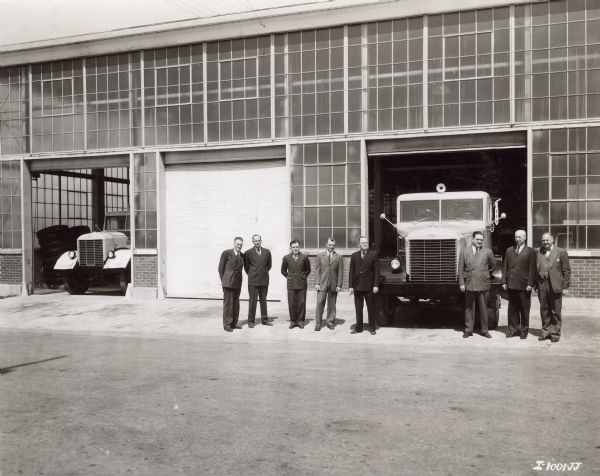 Outdoor group portrait of eight men standing outside of the Emeryville factory with a truck parked in the open doorway. Another truck is parked in an open doorway on the left. Caption reads: "The first four heavy-duty 'Western' models produced at International Harvester's Emeryville, Calif., Works were these 215-inch wheelbase model W-4064-H unites built for International Cementers, Inc., of Long Beach, California. Oil well cementing equipment will be mounted on these units. Individuals in the picture are, left to right: H. E. Straub, General Foreman; E. H. Bickell, Material Controller; E. C. Becker, Buyer; R. F. Hagens, Employment and Industrial Relations Manager, F. C. Miller, Auditor; and A. W. Engstrom, Works Manager. All of Emeryville Works."