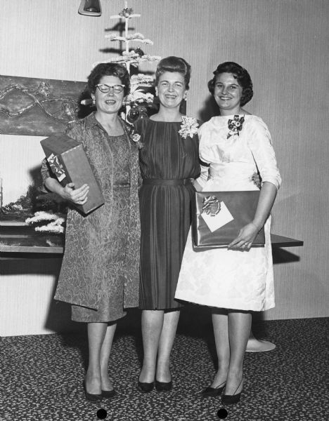 Three women posing with wrapped gifts. Typewritten notes about event from J. W. Vance: "As the Group left the room at the end of the Luncheon program 1:45 P.M.), Christmas wrapped SCOUT kits were distributed by three young ladies of the District Office and Public Relations Staff."