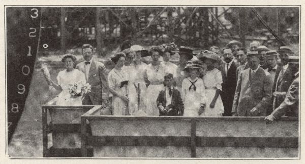 A group portrait of the formally attired launching party about to christen the ship S.S. <i>Harvester</i> on the day she was launched. The woman on the left holds a champagne bottle at the ready.