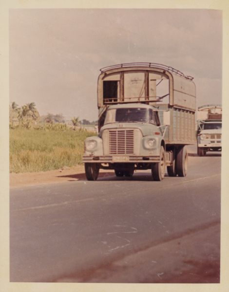 International truck on a road in Vietnam. Another truck is behind on the right. The trucks were used to haul goods from the different provinces to Saigon, a city of three million people, many of whom have fled their country homes to the city because of the war.  Report states: "Trucks used to carry vegetables from Da Lat (Central Highlands) to Saigon, over a distance of 300 kilometers. To travel from Da Lat to Saigon takes 6.5-7 hours. The roads are in good-fair condition." Description of equipment: City: Cholon. Loadstar 1700, 3 years old, standard; RA-146 Used."