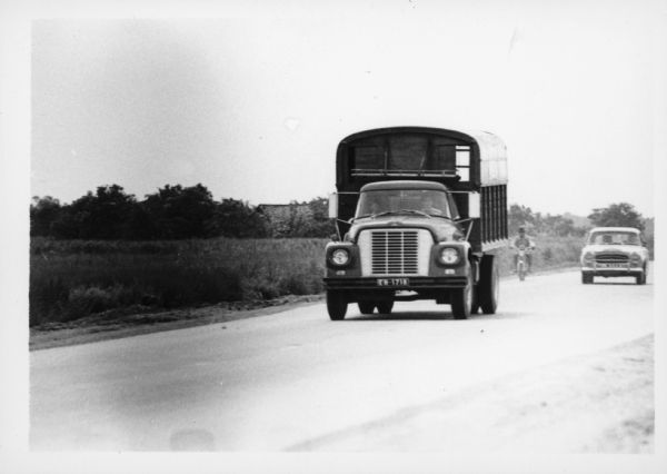 A man is driving an International Harvester truck on a road in Vietnam. Behind the truck on the right is a man riding a scooter, and another person is driving an automobile. The trucks were used to haul goods from the different provinces to Saigon, a city of three million people, many of whom have fled their country homes to the city because of the war. Report states: "Trucks used to carry vegetables from Da Lat (Central Highlands) to Saigon, over a distance of 300 kilometers. To travel from Da Lat to Saigon takes 6.5-7 hours. The roads are in good-fair condition." Description of equipment: City: Saigon. Loadstar 1700, 3 years old.