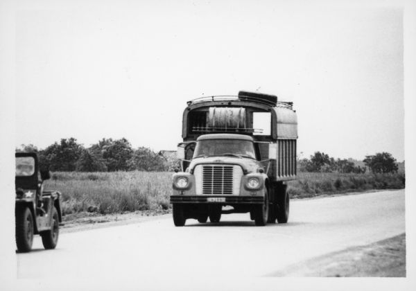 A man is driving an International Harvester truck on a road in Vietnam. A man driving a jeep is in front of the truck on the left. The trucks were used to haul goods from the different provinces to Saigon, a city of three million people, many of whom have fled their country homes to the city because of the war. Report states: "Trucks used to carry vegetables from Da Lat (Central Highlands) to Saigon, over a distance of 300 kilometers. To travel from Da Lat to Saigon takes 6.5-7 hours. The roads are in good-fair condition." Description of equipment: City: Saigon. Loadstar 1700, 3 years old.