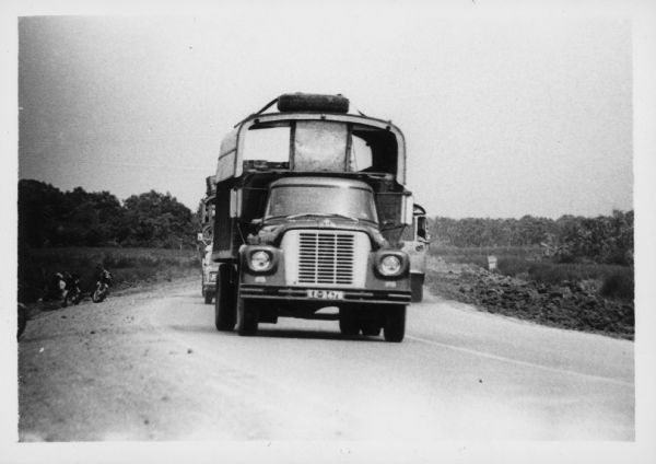 A man is driving an International Harvester truck on a road in Vietnam. Scooters or motorcycles are parked on the side of the road on the left. The trucks were used to haul goods from the different provinces to Saigon, a city of three million people, many of whom have fled their country homes to the city because of the war. Report states: "Trucks used to carry vegetables from Da Lat (Central Highlands) to Saigon, over a distance of 300 kilometers. To travel from Da Lat to Saigon takes 6.5-7 hours. The roads are in good-fair condition." Description of equipment: City: Saigon. Loadstar 1700, 4 years old.