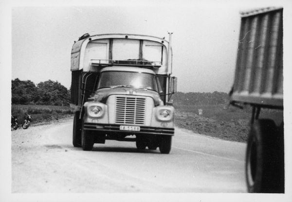 International Harvester truck on a road in Vietnam. Another truck is in front of the IH truck in the foreground on the right. Two motorcycles or scooters are parked on the left side of the road. The trucks were used to haul goods from the different provinces to Saigon, a city of three million people, many of whom have fled their country homes to the city because of the war. Report states: "Trucks used to carry vegetables from Da Lat (Central Highlands) to Saigon, over a distance of 300 kilometers. To travel from Da Lat to Saigon takes 6.5-7 hours. The roads are in good-fair condition." Description of equipment: City: Saigon. Loadstar 1700, 3 years old.