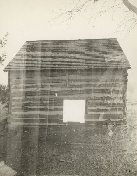 Exterior view of side of a log building with a peaked roof. There is a large opening in the center near the ground.