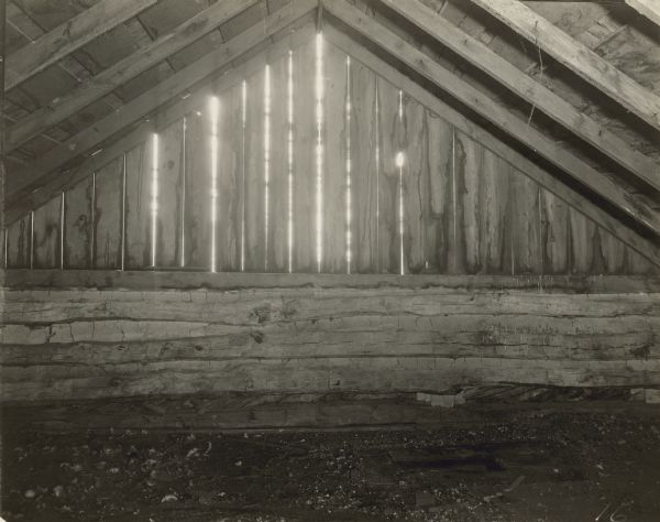 Interior view of log building, with peaked roof. Daylight is coming through the wall boards.