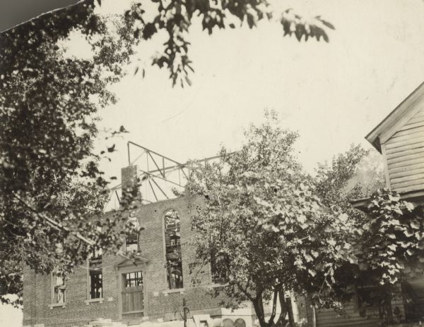 View towards a brick building under construction with the frames for the roof exposed. The corner of another building is on the right.