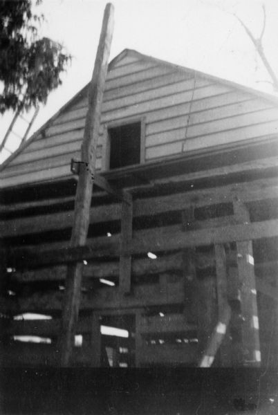 View of the end of the building showing scaffolding around the the log walls, and the peaked roof above. Handwritten on back: "Slave Quarters in process of Restoration."