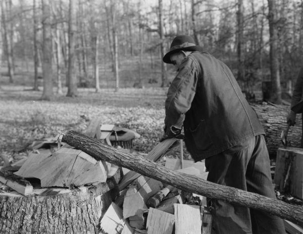 A man is making split shingles. Handwritten on back: "5. A thin section of block being split to shingle thickness with the aid of the frow[sic]."