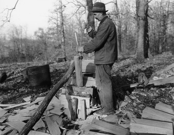 Man standing outdoors using a frow to split shingles.
