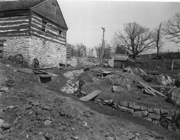 Handwritten on back: "Lower end of tail race." The Blacksmith Shop is on the far left, and the reconstruction of the mill is just behind it. In the center background a man is standing on the bridge.