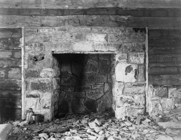 Interior view towards the fireplace. Debris is on the floor. Handwritten on back: "Fireplace first floor of slave cabin. Note old andirons."