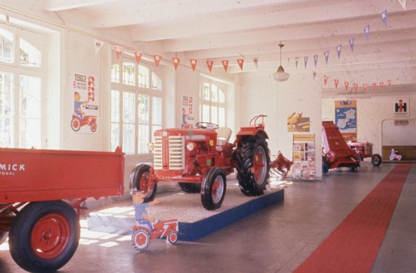 Display room in France. In the center is a McCormick tractor, and other equipment on the left and right. Posters on the wall read: "1962 6 Nouveaux Tracteurs." 
