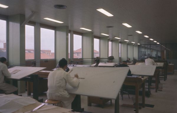 View towards men working at drafting tables near windows.