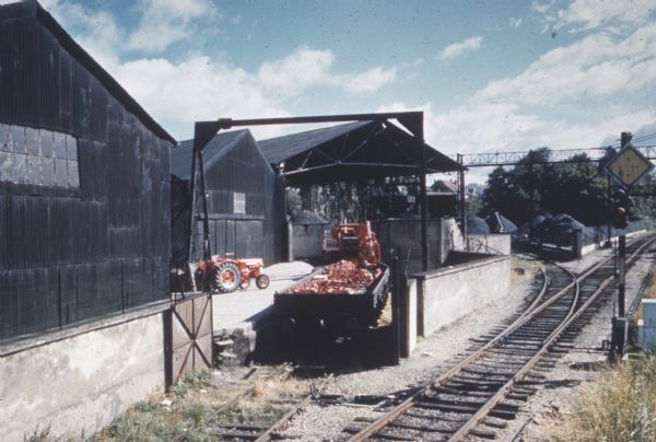 View across railroad tracks toward buildings, a tractor, and a loading dock.