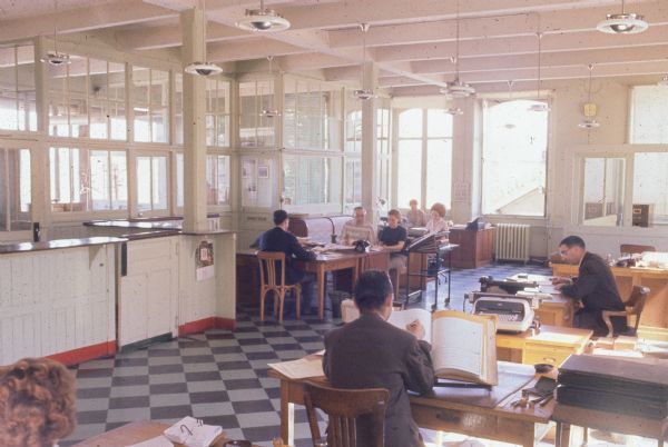 A group of men and women are working at desks in an office.