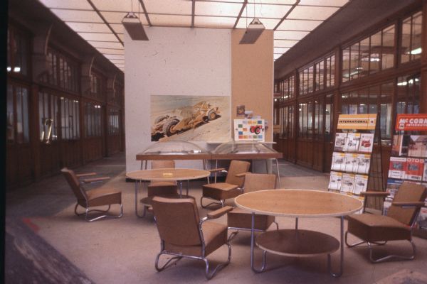 Interior view of tables and chairs in the atrium of an office setting. There is a large poster and photographs on a wall in the center. Ont he right are racks of literature for International and McCormick International on the right.
