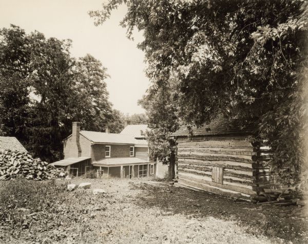 View down hill towards the slave cabin on the right, and the manor house in the background. On the left is a pile of fuelwood.