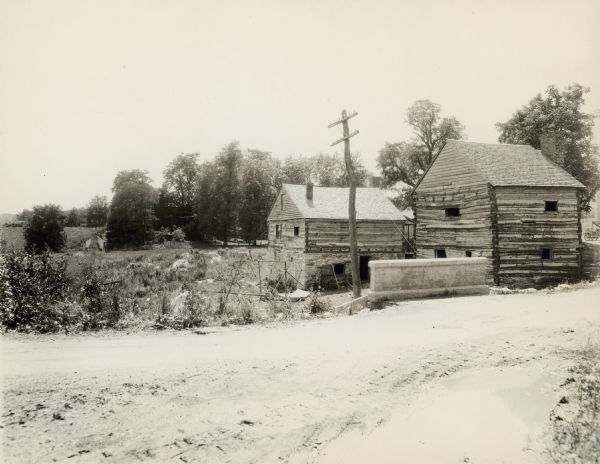 View down road toward the mill building and blacksmith shop at Walnut Grove farm. In the background on the right is a silo. In the background on the left is the spring house with an external chimney.