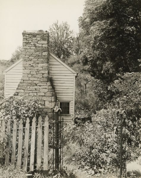View toward the Spring House at the base of a hill. A fence and gate are in the foreground.