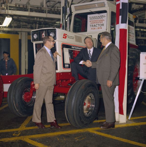 The 5,000,000th International Harvester tractor to roll off the assembly line on Feb. 1, 1974. The tractor is a Farmall 1066. Three men are standing in front of the tractor. Two men on the right are shaking hands, and the man on the left is looking on and holding a cigar.