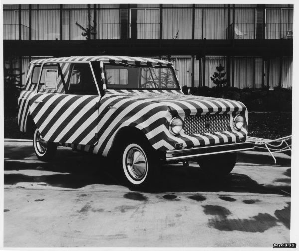 Three-quarter right side view of a IH Scout with a black and white Zebra exterior. Photograph contains presumably the negative number myk-3133 but is cut off before a date listing. Records indicate the photograph was taken between 1961-1977. A sheet of paper attached to the partially opened passenger side door is titled: "Delivered Price."