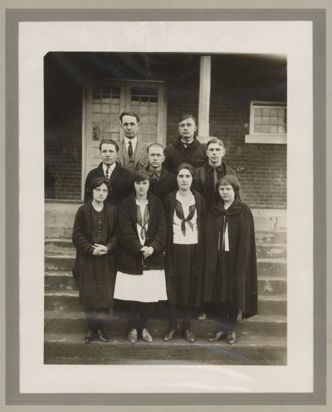 Outdoor group portrait of nine people posing on the steps of a building.